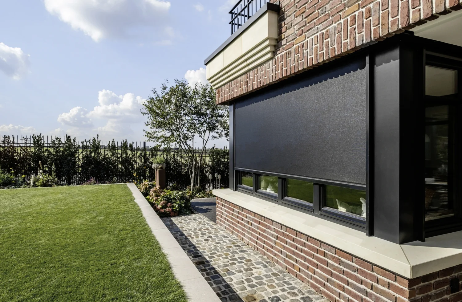 Moderne Sonnenblende an einem Backsteinhaus mit gepflegtem Garten